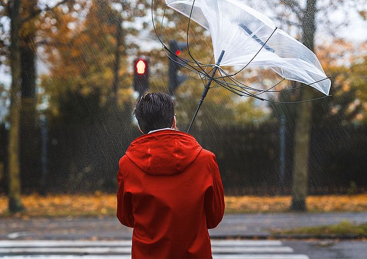 Mann geht mit Regenschirm der durch starken Wind umgebogen wird.