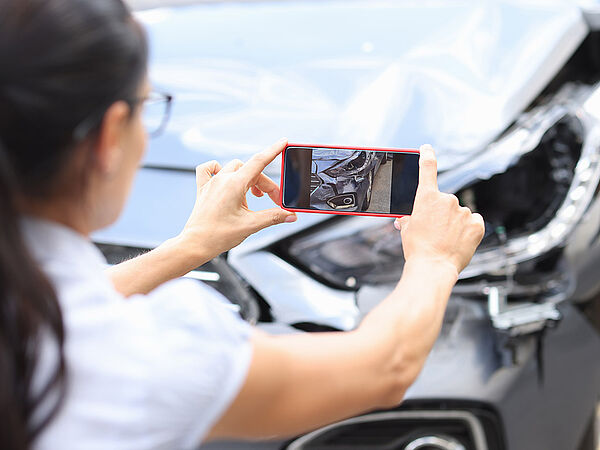 Eine Frau macht mir ihrem Smartphone ein Foto vom entstandenen Schaden an ihrem Auto.