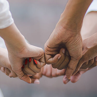 Mehrere unterschiedliche Hände mit geballten Fäusten treffen sich in der Mitte des Bildes