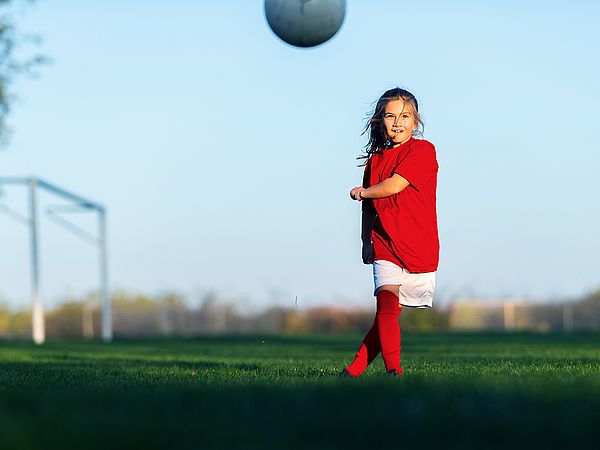 Ein junges Mädchen in Fußballtrikot schießt einen Ball auf einem Fußballfeld 