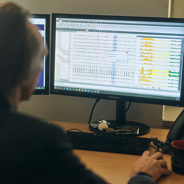 Ein Forscher sitzt vor einem Monitor. Darauf zu sehen bunte Kurven und Phasen. 