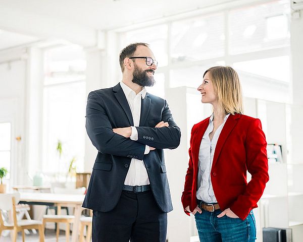 Eine Geschäftsfrau und ein Geschäftsmann stehen nebeneinander im Büro und lächeln sich an