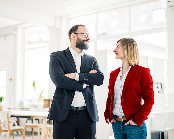 Eine Geschäftsfrau und ein Geschäftsmann stehen nebeneinander im Büro und lächeln sich an
