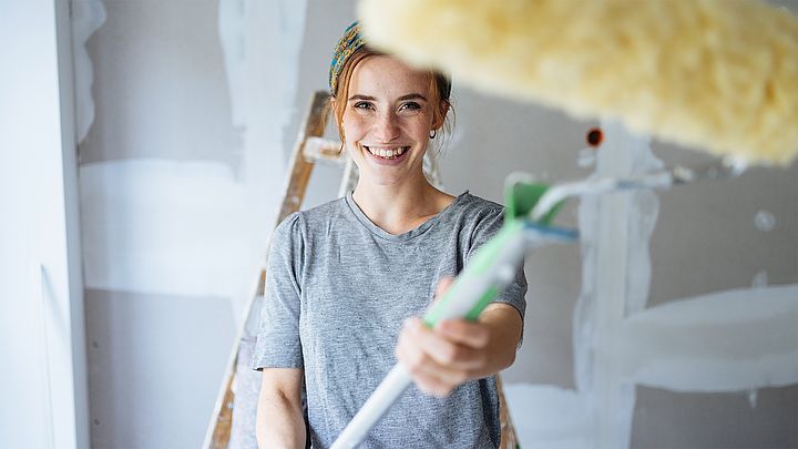 Junge Frau lächelt und hält eine Malerwalze in der Hand.