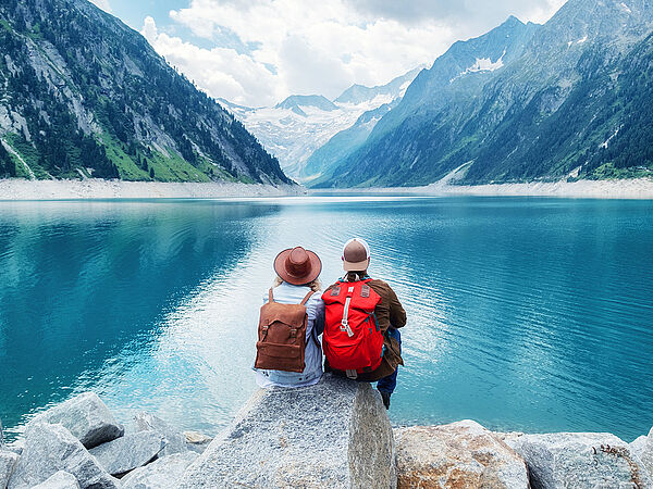 Ein Paar in Wanderkleidung sitzt auf einem Felsen und blickt auf einen See in den Bergen