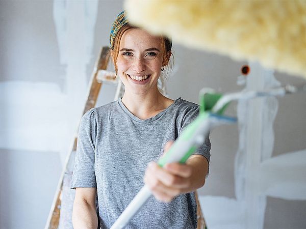 Junge Frau lächelt und hält eine Malerwalze in der Hand.