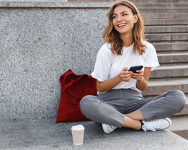 Eine junge Frau sitzt auf Treppen im Freien und tippt auf ihrem Smartphone.