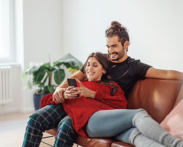 Eine junge Frau liegt auf dem Schoß ihres Partners und beide blicken auf ihr Smartphone.