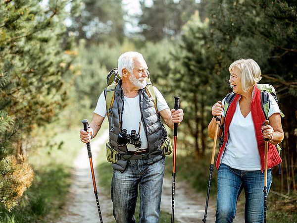 Ein glückliches Seniorenpaar wandert mit Nordic-Walking-Stöcken durch den Wald.