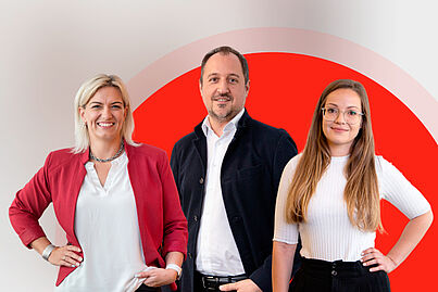 Zwei Damen und ein Herr lächeln in die Kamera.