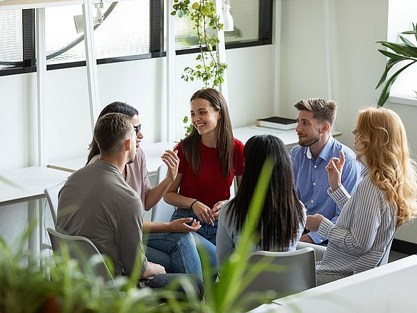 Eine Gruppe von jungen Leuten sitzt im Büro im Kreis und bespricht etwas.