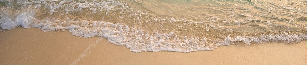 Sanfte Wellen eines türkisblauen Meeres rollen über einen hellen Sandstrand bei ruhigem, klarem Wetter