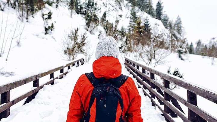 Eine Frau wandert mit einem Rucksack über eine Brücke in einer Winterlandschaft.