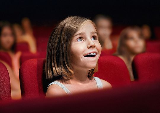 Ein Mädchen sitzt im Kinosaal und schaut gespannt auf die Leinwand