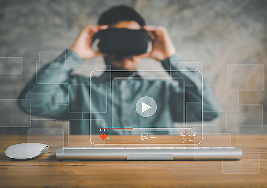 Ein Mann trägt eine VR Brille. Dabei erscheint direkt vor ihm ein digitaler Bildschirm. 