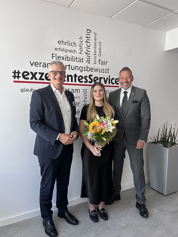 Zwei Herren und eine junge Dame, die einen Blumenstrauß in den Händen hält.