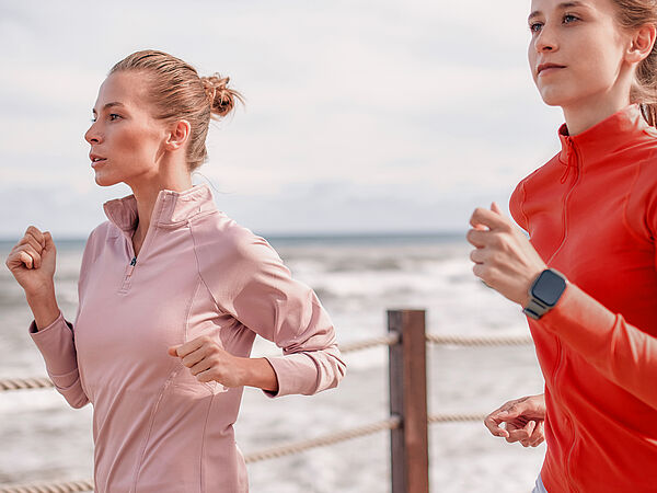 Zwei junge Damen joggen entlang des Meeresufers.