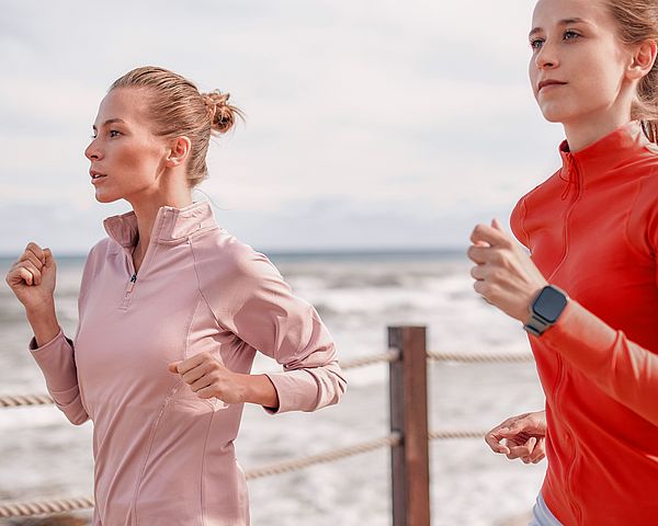 Zwei junge Damen joggen entlang des Meeresufers.