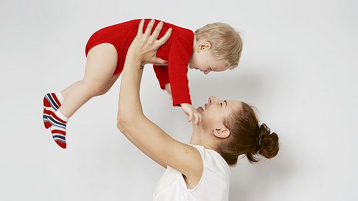 Eine junge Frau hält ein Kleinkind in die Höhe und beide lachen.