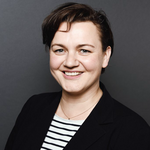 Porträtfoto einer Frau mit kurzen dunklen Haaren. Sie trägt ein schwarzes Sakko und ein gestreiftes Shirt und lächelt.