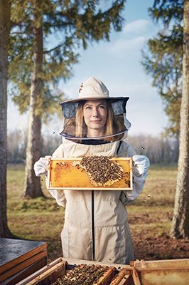 Eine Imkerin steht im Wald bei ihren Bienenvölkern und zeigt Honigwaben in die Kamera 