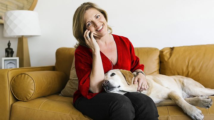 Eine glückliche Frau telefoniert während ihr Hund auf ihrem Schoß liegt.