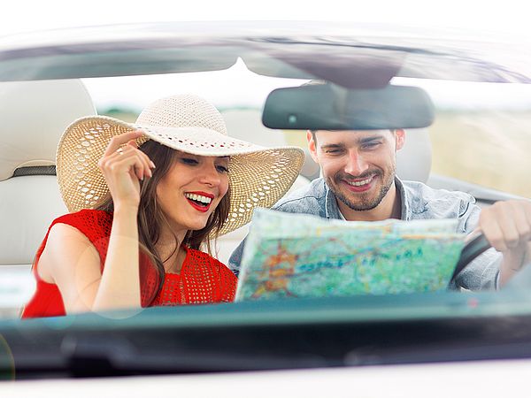 Junges glückliches Paar sitzt im Auto und liest eine Landkarte.