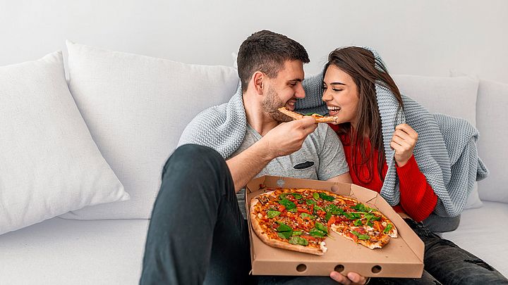 Ein junges Paar isst zu Hause eine Pizza auf der Couch.