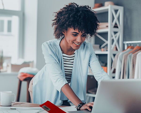 •	Eine Frau arbeitet in einem Büro am Laptop auf einem unaufgeräumten Tisch 