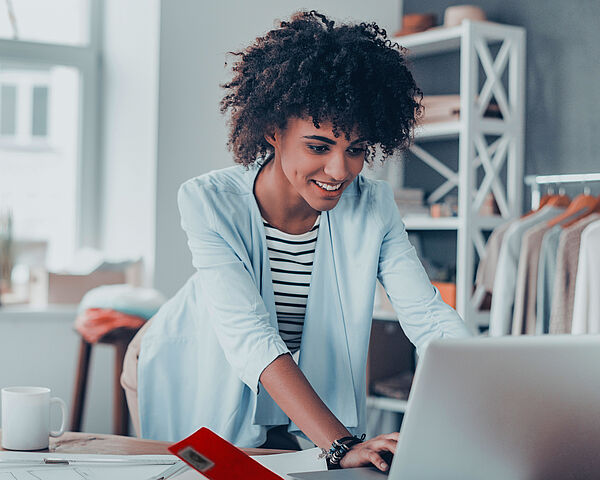 •	Eine Frau arbeitet in einem Büro am Laptop auf einem unaufgeräumten Tisch 