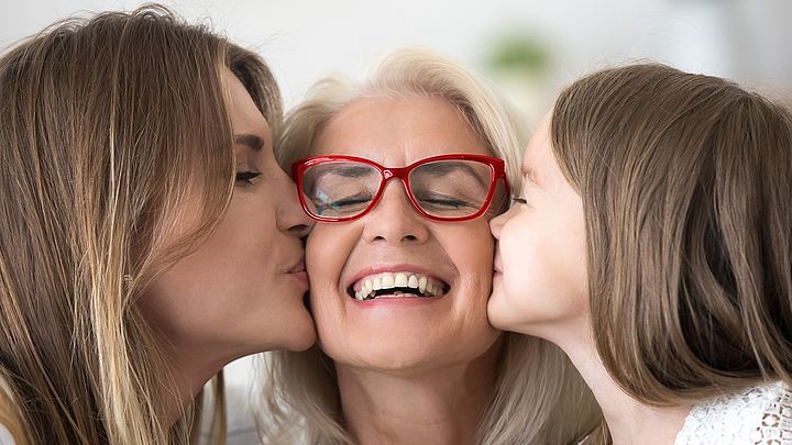 Eine glückliche ältere Frau wird von ihrer Tochter und ihrer Enkeltochter auf die Wange geküsst.