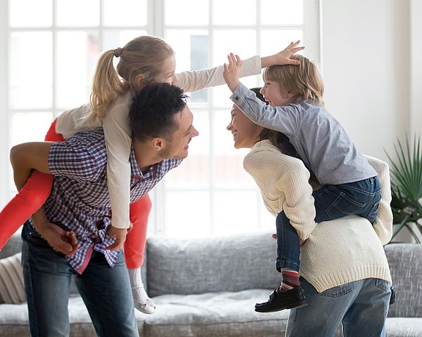 Die jungen glücklichen Eltern tragen ihre Kinder auf dem Rücken.