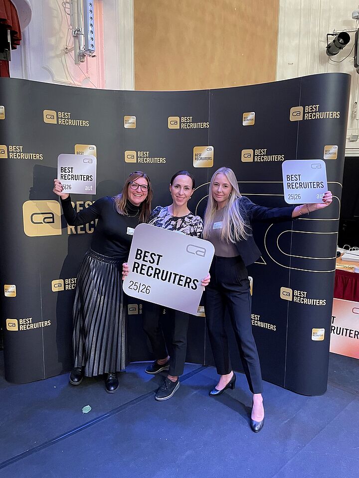 Gruppenfoto auf der Bühne bei der Best-Recruiters Verleihung. Drei Personen halten die Auszeichnung freudig in die Kamera.