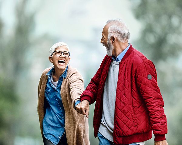 Ein glückliches Seniorenpaar geht Hand in Hand im Wald spazieren.