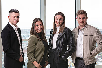 Vier Mitarbeiter stehen zusammen und lächeln in die Kamera.