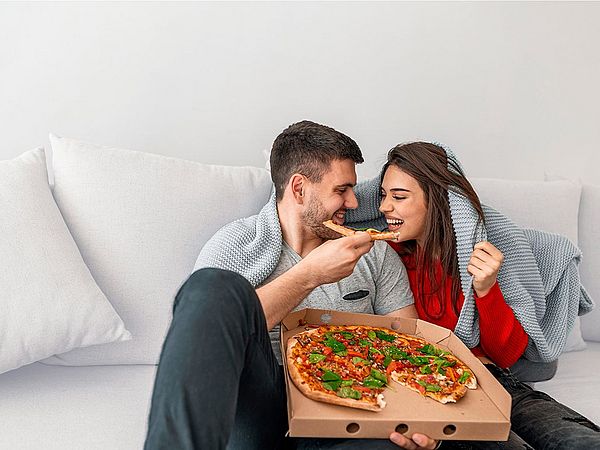 Ein junges Paar isst zu Hause eine Pizza auf der Couch.