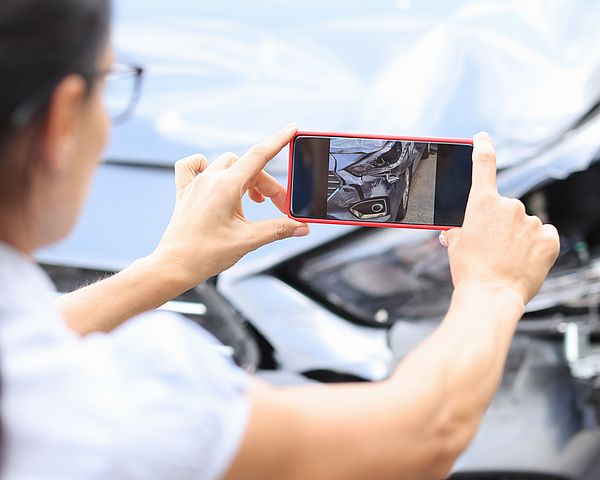 Eine Frau macht mir ihrem Smartphone ein Foto vom entstandenen Schaden an ihrem Auto.