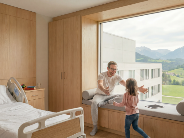 Ein Mann sitzt lachend auf einer Fensterbank und breitet die Arme aus, während ein kleines Kind auf ihn zuläuft, in einem hellen, modernen Raum.