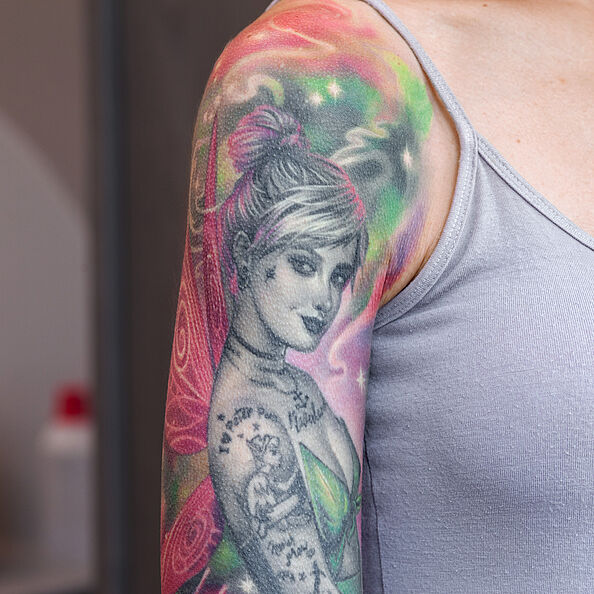 Oberarm mit großflächigem, buntem Tattoo, das eine Frau mit Flügeln zeigt