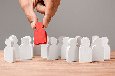 Hand hebt rote Spielfigur in die Höhe, daneben stehen weiße Spielfiguren.