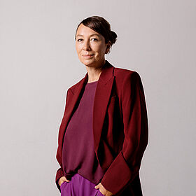 Schauspielerin Ursula Strauss steht mit lächelndem Blick in die Kamera und Händen in den Hosentaschen.