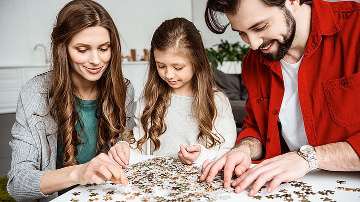 Ein junges Paar baut mit seiner Tochter ein Puzzle am Wohnzimmertisch.