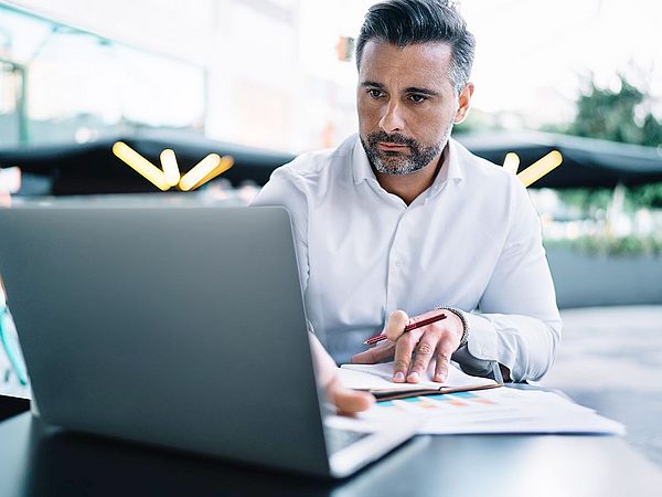 Ein Geschäftsmann sitzt am Schreibtisch vor seinem Laptop und macht sich konzentriert Notizen 