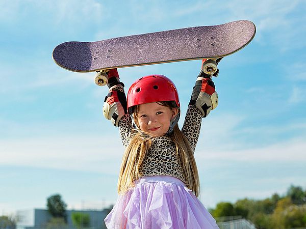 Bild aus Werbespot: Mädchen hebt Skateboard hoch über den Kopf.