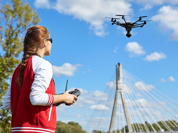 Junge Frau mit Sonnenbrille und roter sportlicher Weste steuert eine Drohne