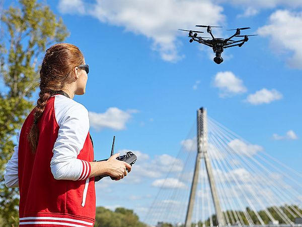 Junge Frau mit Sonnenbrille und roter sportlicher Weste steuert eine Drohne