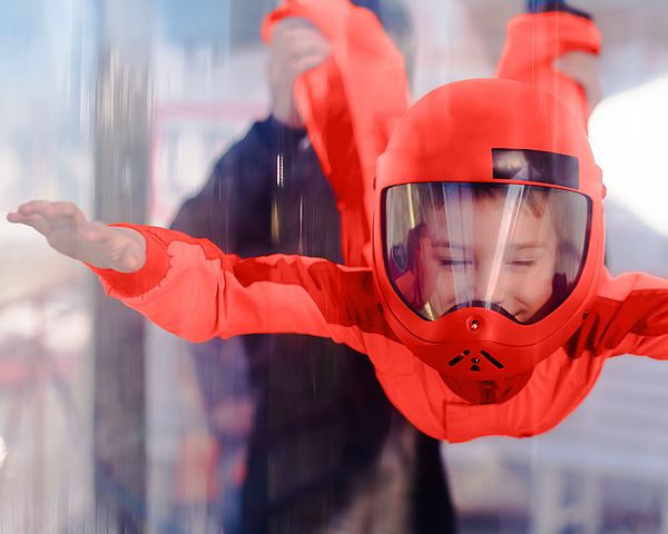 Kind fliegt mit rotem Anzug in einem Windkanal und lacht.