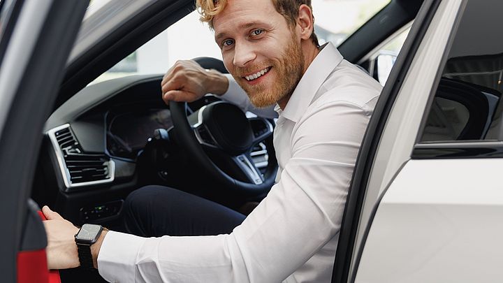 Ein glücklicher Mann im Hemd öffnet die Tür und steigt aus dem Auto aus.