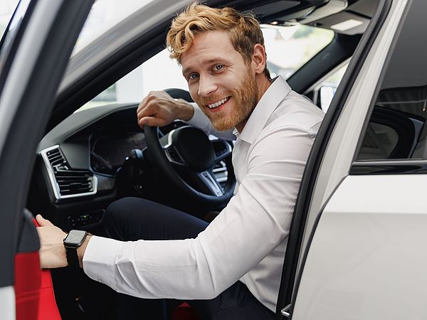 Ein glücklicher Mann im Hemd öffnet die Tür und steigt aus dem Auto aus.