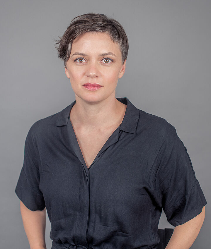 Foto von einer Frau mit kurzen braunen Haaren in dunkler Kleidung mit kurzen Ärmeln